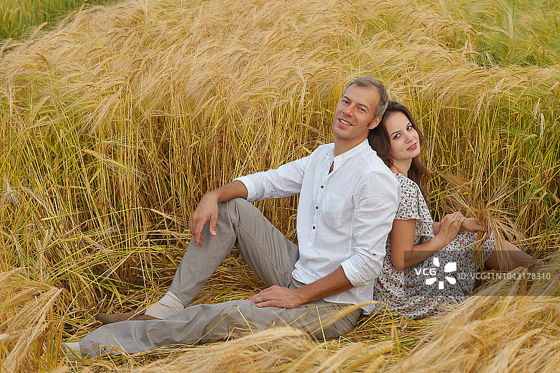 一对幸福的夫妇坐在麦田里的草地上图片素材