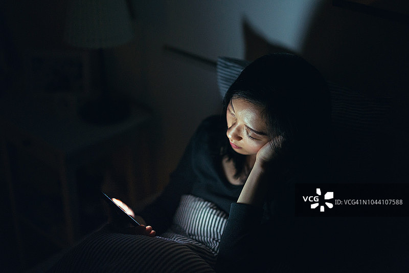 疲惫的女人晚上在床上使用智能手机时睡着了图片素材