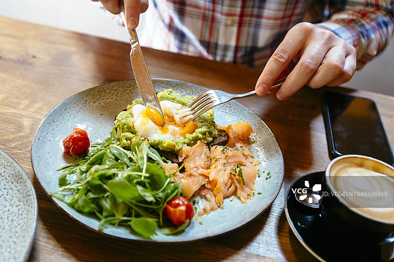 一名男子在餐厅吃早午餐，吃牛油果吐司配鸡蛋、鲑鱼和芝麻菜沙拉图片素材