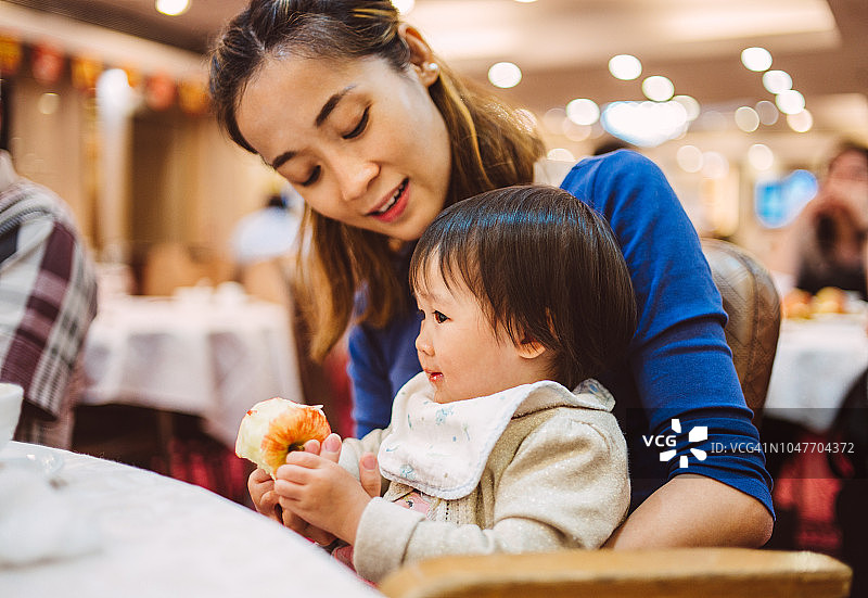 年轻漂亮的妈妈和蹒跚学步的小女孩在一家传统的中国餐馆愉快地享用苹果。图片素材