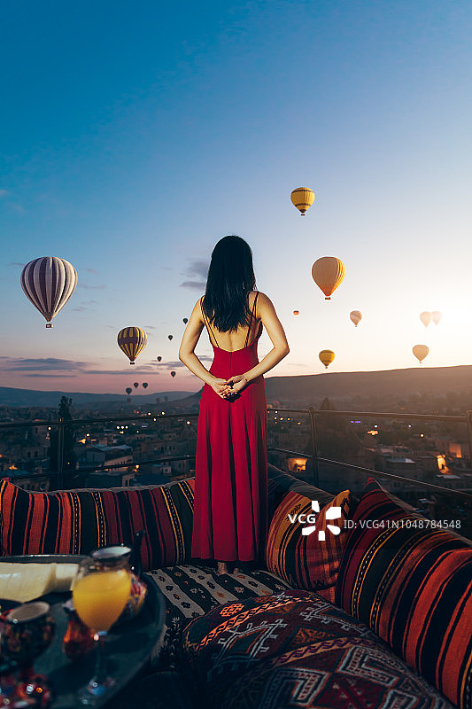 美丽的亚洲女人看彩色的热气球飞过卡帕多西亚，土耳其山谷的背影。土耳其卡帕多西亚童话般的山景。土耳其卡帕多西亚童话般的山景。图片素材