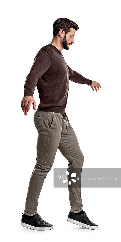 在白色的背景下，一个穿着休闲衣服的健康男子抬起他的脚，在走钢丝的过程中向下看。图片素材