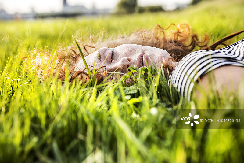红发年轻女子的肖像，闭着眼睛躺在草地上图片素材