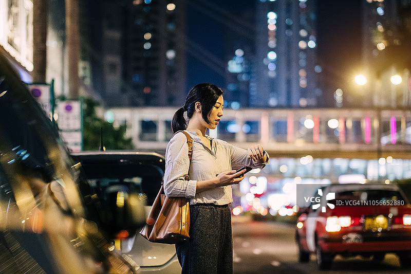 年轻女子用手机查看手表时间在繁忙的街道在城市晚上图片素材