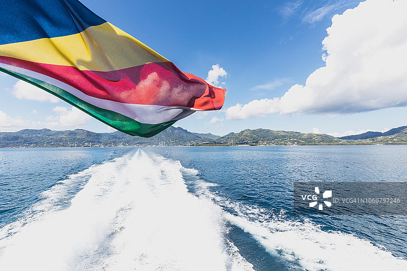 在大海和一个岛屿前挥舞的塞舌尔旗帜的特写。图片素材