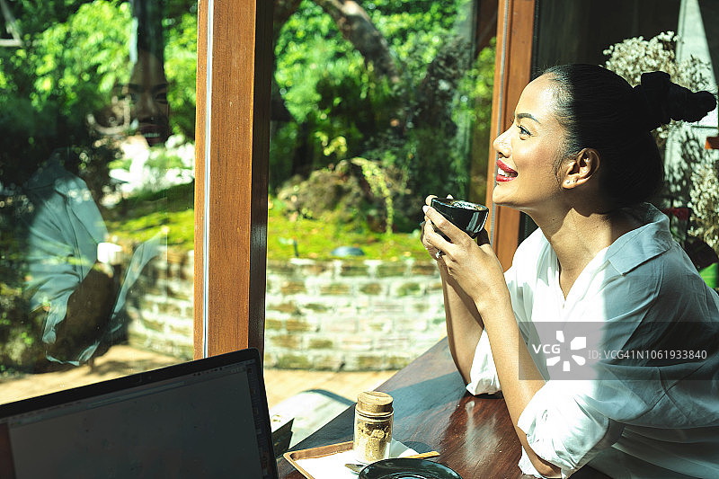 一幅漂亮女人拿着杯子透过窗户看咖啡的画像。图片素材