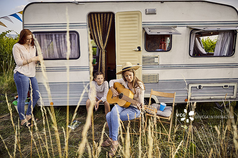 母亲和两个女儿坐在大篷车外面弹吉他图片素材