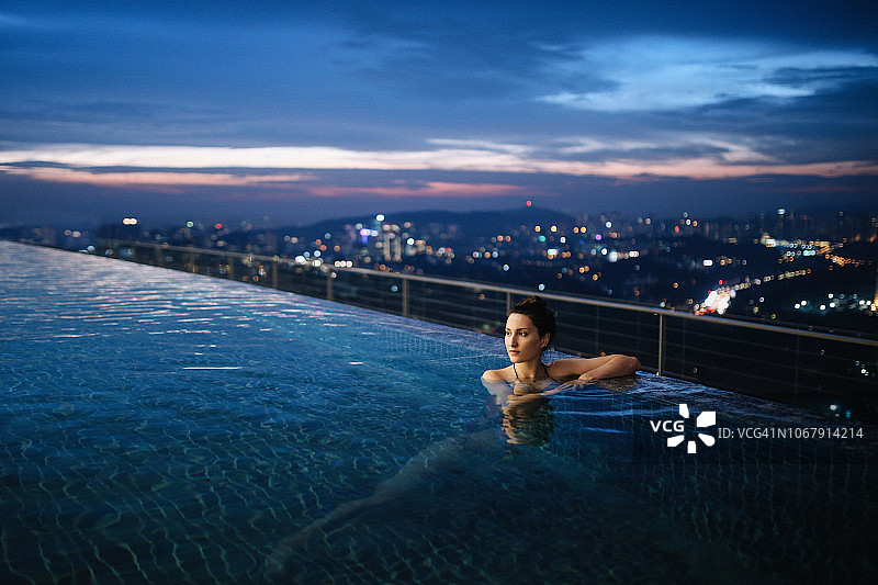 年轻女子有一个晚上游泳在马来西亚的游泳池图片素材