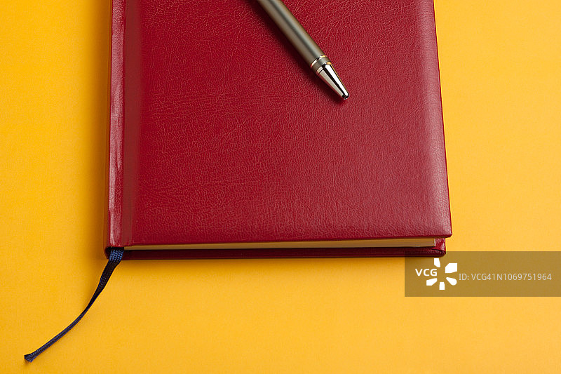 商业时间就是金钱的概念，一个新的漂亮的红色笔记本和一支负责任的人用的钢笔在明亮的黄色背景上图片素材
