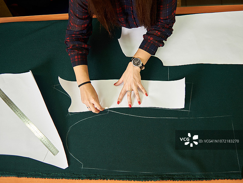 在工作室制作工作台。女性的双手在绿色织物上用粉笔画出纸的图案。图片素材