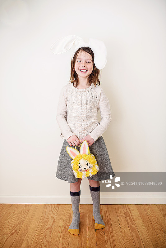 一个微笑的女孩戴着兔子耳朵拿着兔子包的肖像图片素材