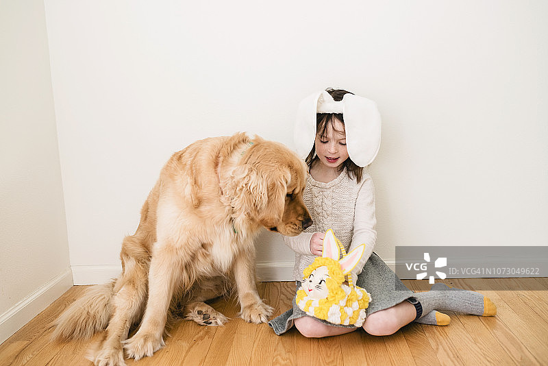 一个带着兔子耳朵的微笑女孩和她的狗坐在地板上的肖像图片素材