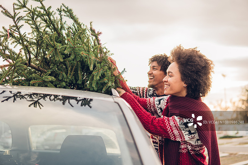 微笑的夫妇将圣诞树系在汽车上图片素材