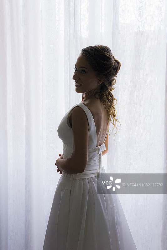 面带微笑的新娘站在家里的窗帘旁图片素材
