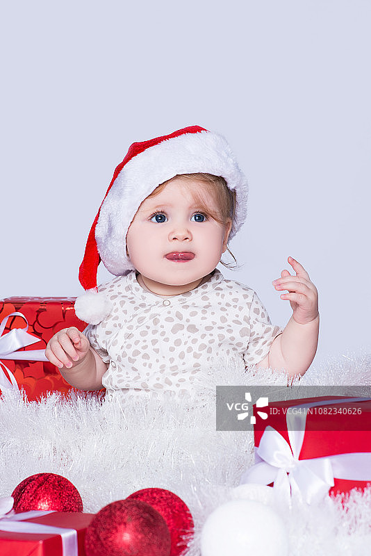 小女孩，戴着圣诞老人的红帽子，周围是圣诞球、礼盒和花环，在灰色的天空中孤立无存图片素材