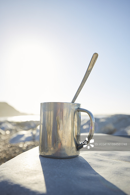 一杯热咖啡，站在海滩边的岩石上图片素材