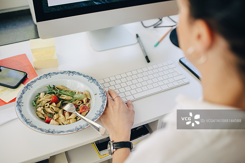 特写的女商人使用电脑，同时在桌子上吃意大利面图片素材