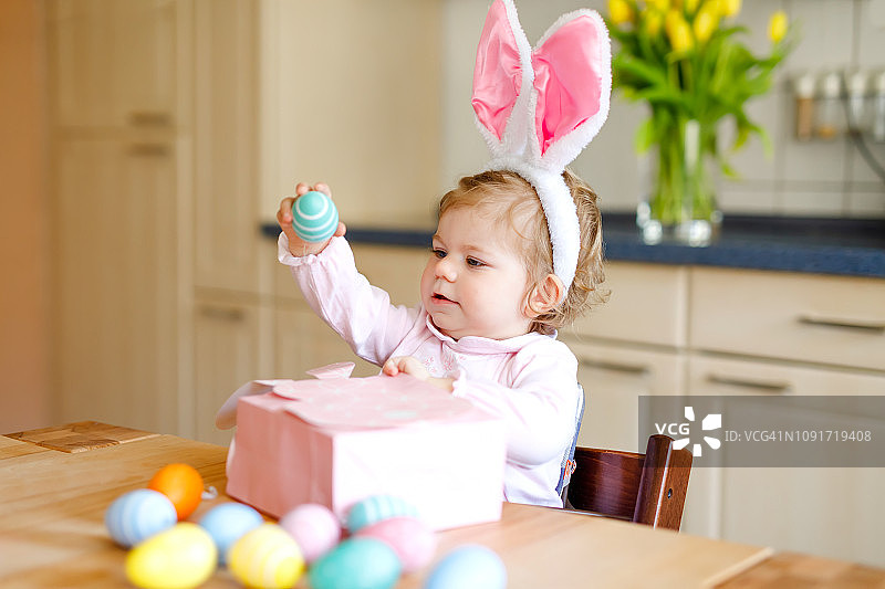 可爱的小女孩戴着复活节兔子耳朵玩彩色彩蛋。快乐宝宝拆礼物。可爱的健康微笑的孩子在粉红色的衣服享受家庭假日图片素材
