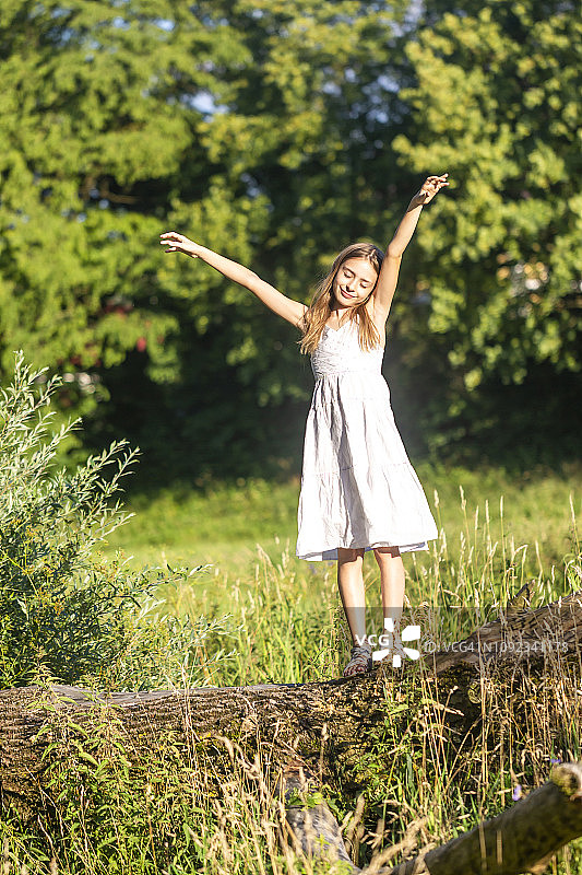 微笑的女孩站在树干上享受阳光的肖像图片素材