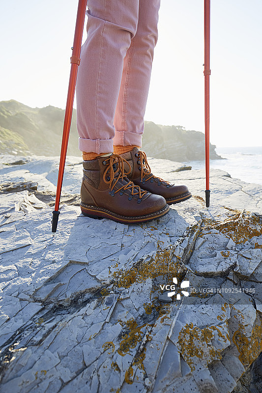 穿着登山靴的女人站在海边的岩石上图片素材