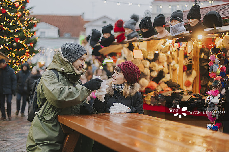 一对日本夫妇在塔林圣诞市场上喝热红酒图片素材