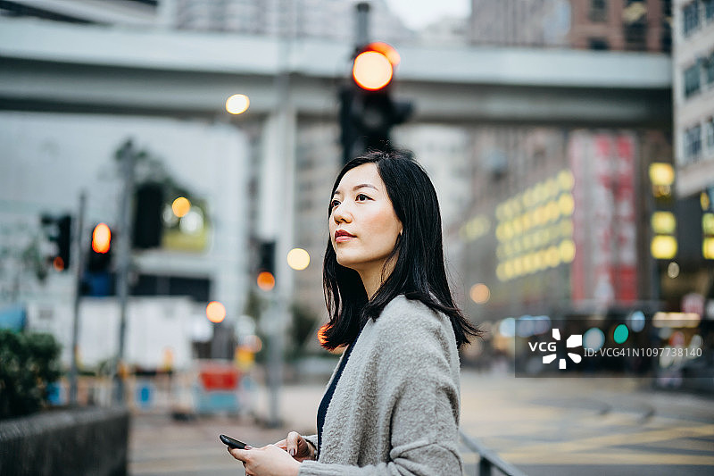 年轻女子用智能手机在城市里通勤，避开繁忙的城市交通和高楼大厦图片素材