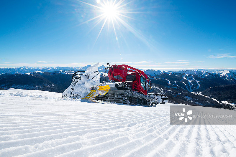 现代的红色雪清理多余的雪从滑雪道，因为太阳照耀明亮图片素材