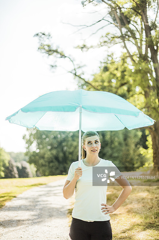 顽皮的年轻女子拿着遮阳伞站在公园里图片素材