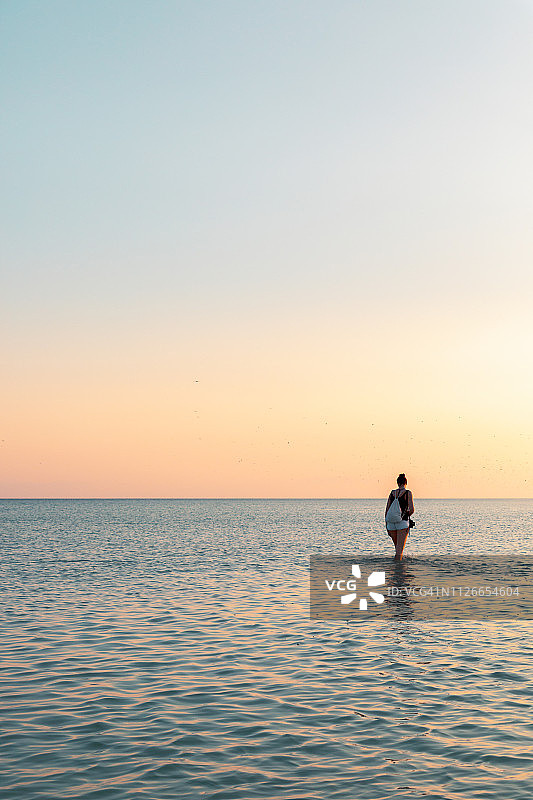 年轻女子站在海里。夏日的日落。图片素材