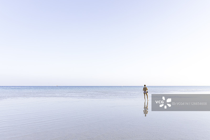 年轻女子站在海滩上望着大海。图片素材