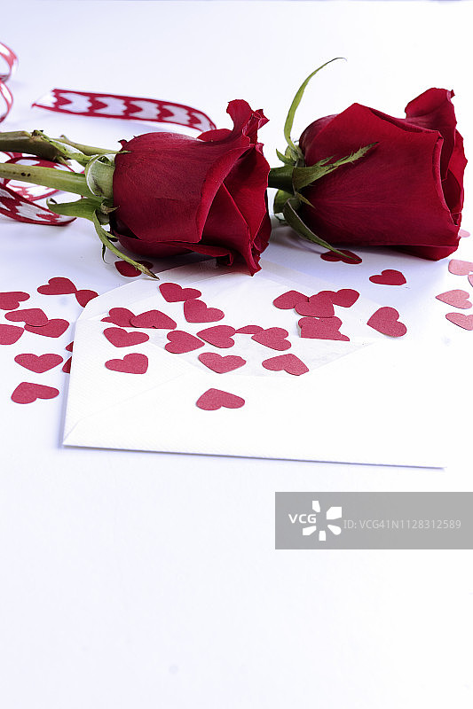 单一空白信封，纸心形状，两朵幽香的深红色玫瑰躺在白色的背景。选择性聚焦和复制空间图片素材
