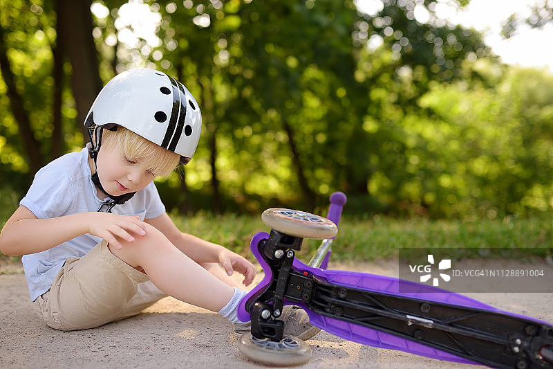 戴安全帽的蹒跚学步的男孩正在学习骑滑板车图片素材