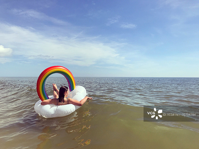 十几岁的女孩漂浮在一个彩虹内胎在海洋图片素材