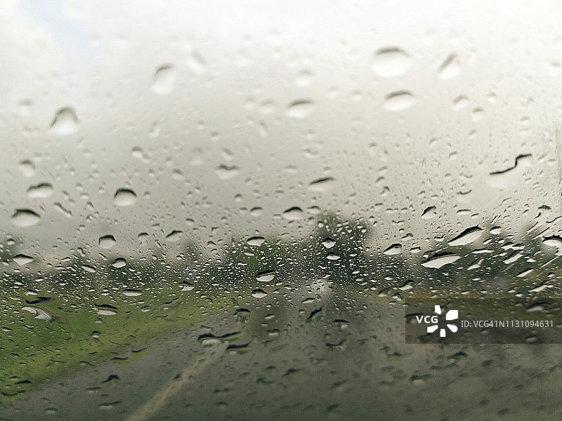 雨点落在汽车玻璃窗上，以雨季道路为抽象背景，水滴落在玻璃上，夜晚暴雨下雨的汽车行驶理念。图片素材