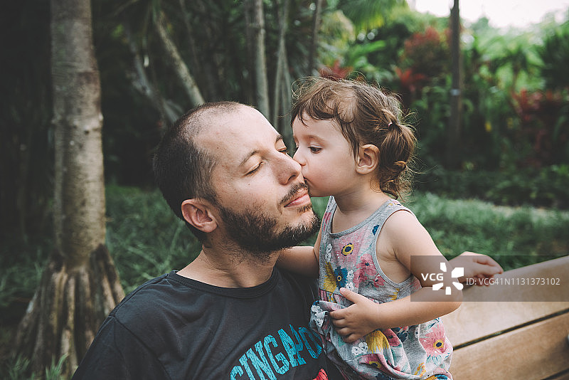 小女孩在公园里亲吻她父亲的脸颊图片素材