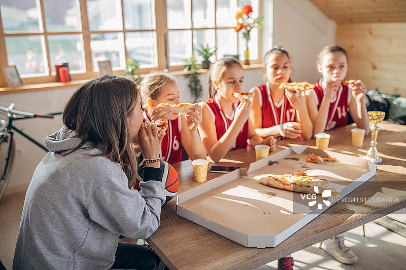 女子篮球运动员在赢得奖杯后和女教练一起吃披萨图片素材