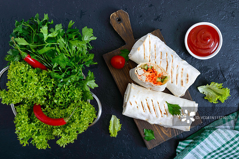 黑色背景上的美味沙瓦玛三明治。墨西哥玉米卷包裹着烤鸡和蔬菜，青菜。墨西哥薄饼、皮塔饼。传统的中东开胃菜。健康食品。俯视图，平放图片素材