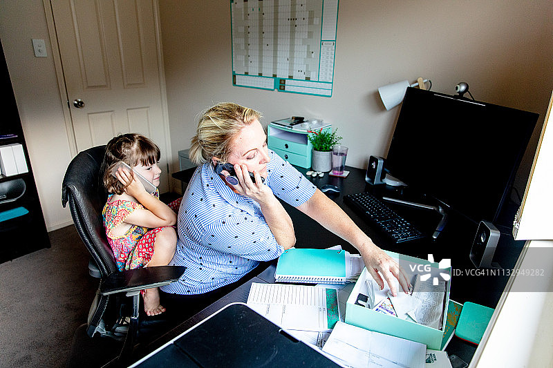 中年妇女在家办公，同时还要照顾年幼的女儿。图片素材