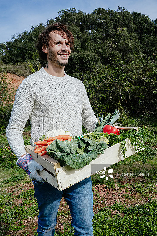 一个男人从他的菜园里搬着一板条箱新鲜收获的蔬菜图片素材