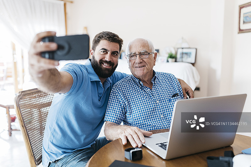 成年的孙子和他的祖父在家里用智能手机自拍图片素材