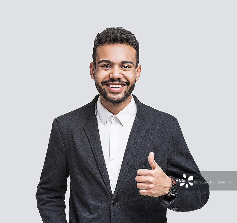 英俊微笑的年轻人竖起大拇指的肖像。图片素材
