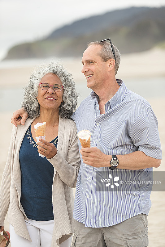 一对老年夫妇在一个美丽的下午沿着海滩散步，一起吃甜筒冰淇淋图片素材