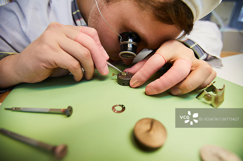 手表工厂的集中工程师戴着单眼放大镜使用镊子组装手表机构的特写图片素材
