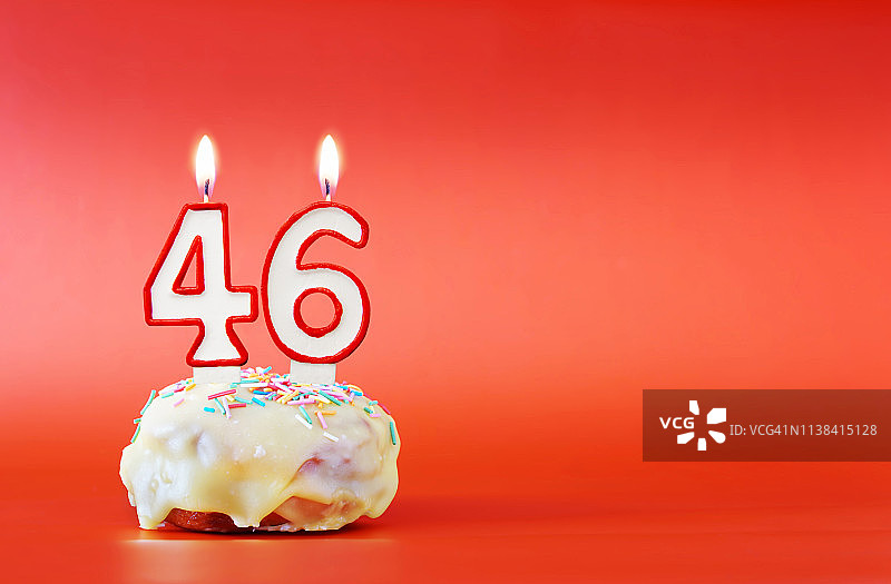 四十六岁生日。纸杯蛋糕，上面有燃烧着的白色蜡烛，数字是46。鲜艳的红色背景与复制空间图片素材