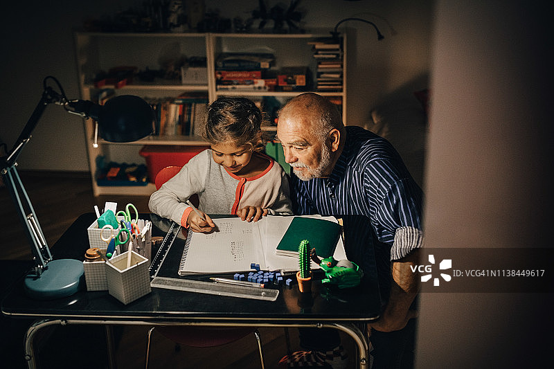 高视角的爷爷和孙女坐在家里的书桌上写作业图片素材