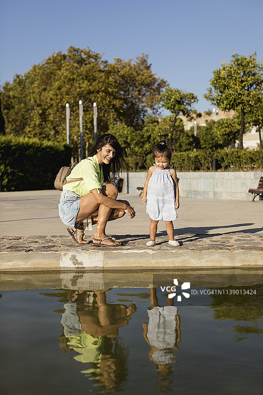 快乐的母亲和女儿在公园水池里看着自己的镜像图片素材