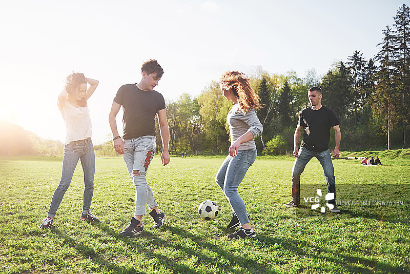 一群穿着休闲服装的朋友在户外踢足球。人们玩得开心，玩得开心。活跃的休息和风景优美的日落图片素材