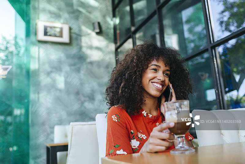 一个快乐的年轻女人的肖像在电话在咖啡店图片素材