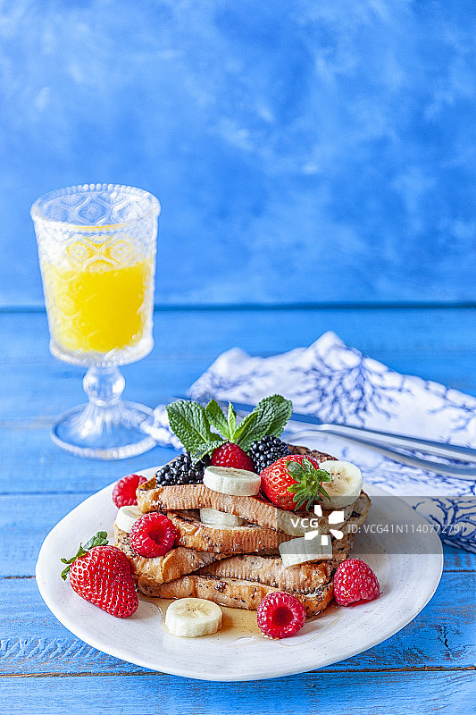 无谷蛋白法式吐司配香蕉，覆盆子，草莓，黑莓和枫糖浆在蓝色的乡村木材背景图片素材