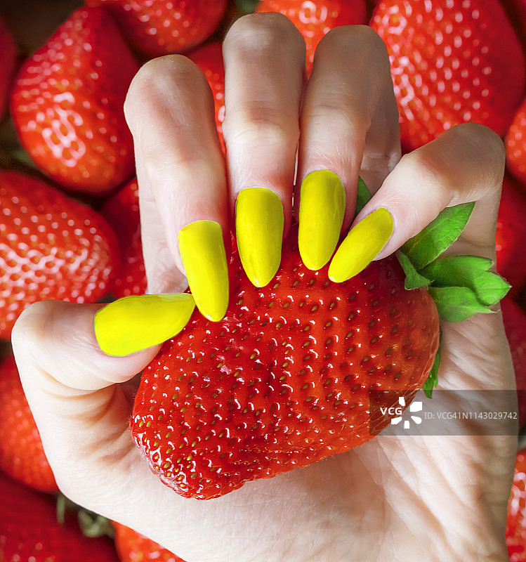 用黄指甲的手捡起一个草莓图片素材
